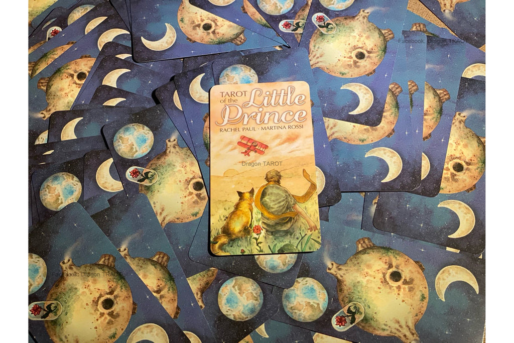 A tarot card deck spread out on a matching patterned surface, with the central card showing 'The Little Prince' artwork and the surrounding cards featuring a blue space design with crescent moons and planets.