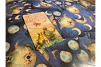 A tarot card deck spread out on a surface, with the 'Little Prince' card prominently displayed in the center. The cards feature a dark blue space background with moon phases and planets, while the central card has an illustration of a turtle and a boy with warm beige and orange tones.