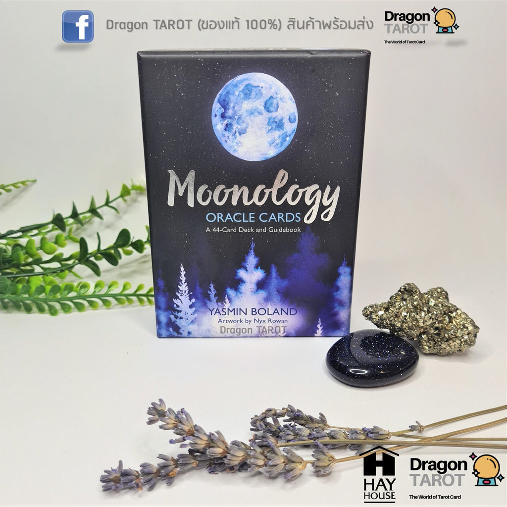 Moonology Oracle Cards deck box shown on a light surface with decorative greenery, a crystal, a black tarot card, and dried lavender sprigs. The box is dark blue with a moon illustration and the title 'Moonology Oracle Cards' visible.