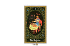 A tarot card titled 'The Magician' shown vertically against a white background. The card features an ornate gold border, a dark green floral frame, and a central illustration of a magician in a blue robe with a red cape, seated at a table with a cauldron.