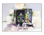 A boxed card deck and a single card displayed on a white surface with decorative white flowers, purple crystals, and a Dragon's Eye logo at the bottom. The box reads 'Nyttilte Night Goddess' and the card shows a colorful illustrated design.