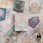 The Rose Oracle card deck box by Rebecca Campbell, displayed on top of a scattered arrangement of its illustrated oracle cards. The box features a light pink and white design with a central rose graphic.
