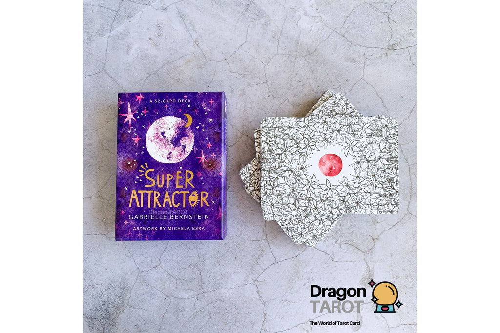 Super Attractor tarot deck by Gabrielle Bernstein, featuring a purple illustrated box and a stack of silver-backed cards with a red circular center, displayed on a light gray stone surface.