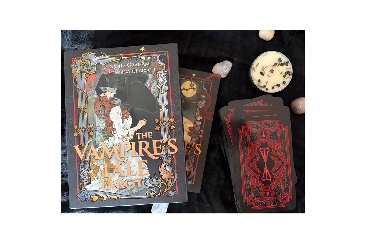 The Vampire's Stall Tarot deck shown with its illustrated box, several face-up cards, and a stack of face-down cards on a dark fabric background, alongside small decorative stones.