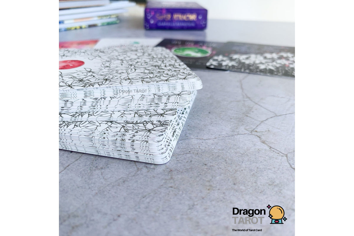 A stack of Dragon Tarot cards with a black and white floral patterned cover sits on a gray stone surface, with other cards and a purple box blurred in the background.