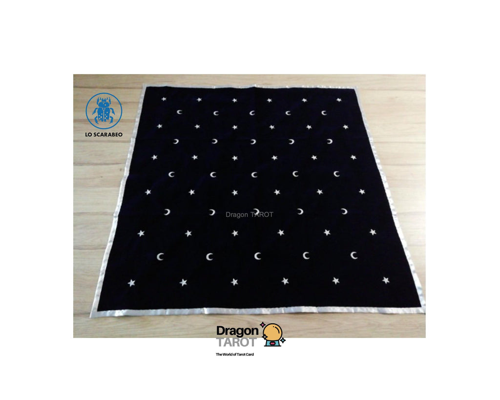A black square tarot card deck cover featuring a celestial pattern of embroidered white crescent moons and stars, laid flat on a light wood floor. The brand logo 'Dragon Tarot' is visible at the bottom of the image.
