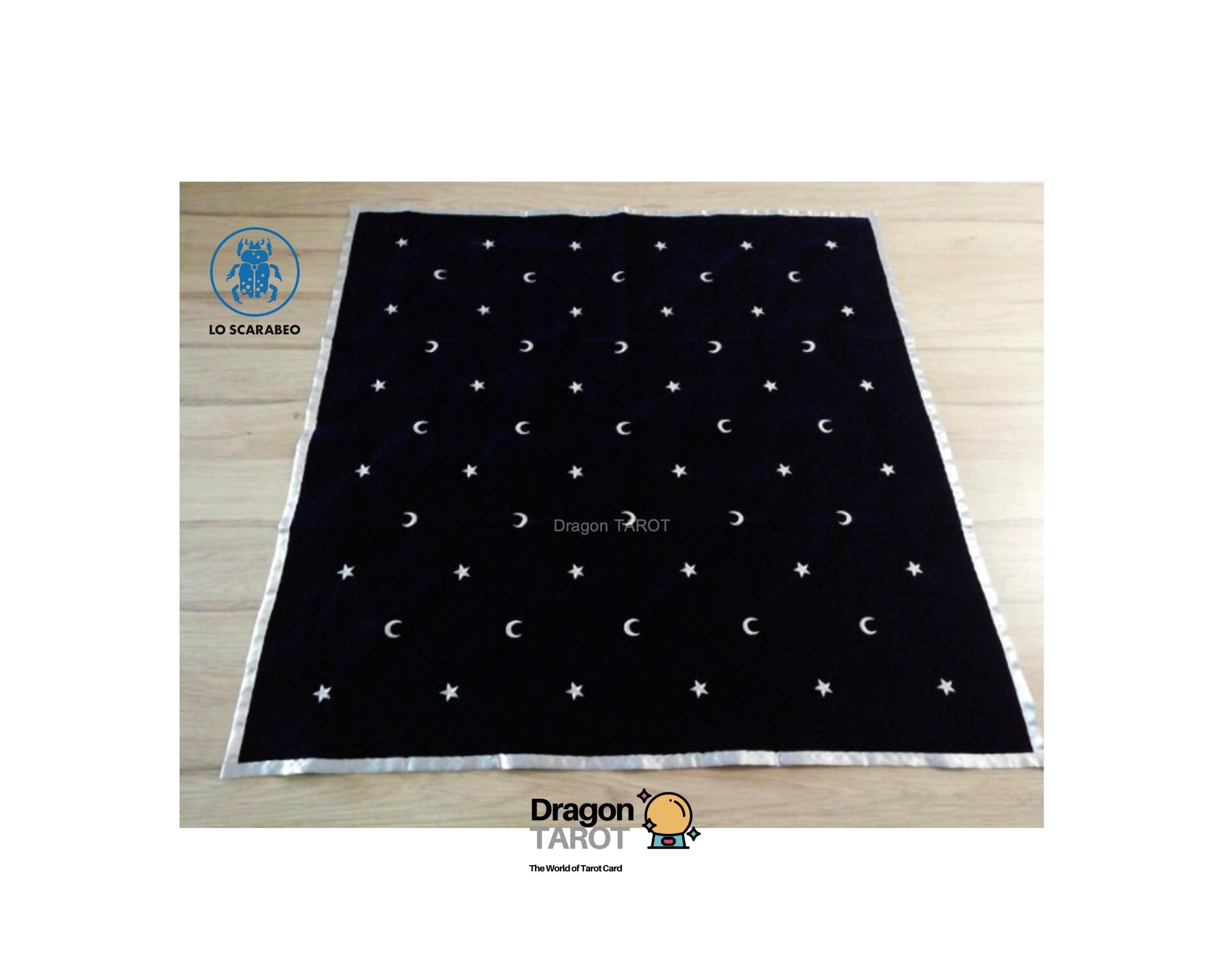 A black square tarot card deck cover featuring a celestial pattern of embroidered white crescent moons and stars, laid flat on a light wood floor. The brand logo 'Dragon Tarot' is visible at the bottom of the image.