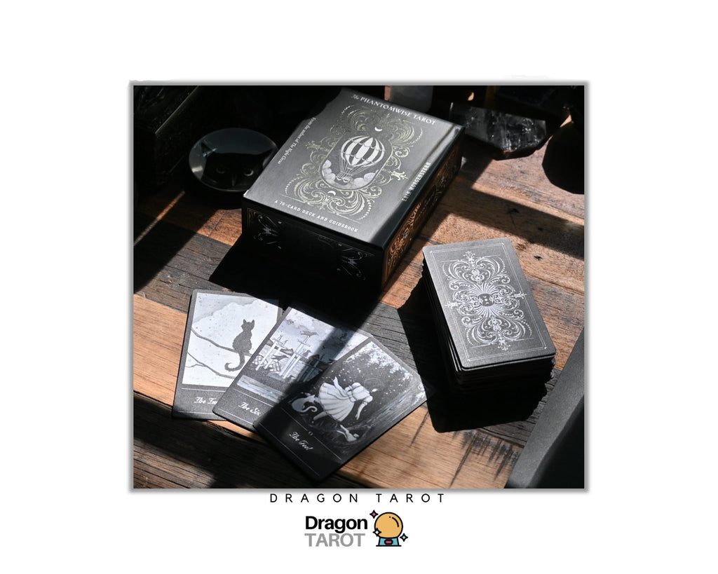 Dragon Tarot deck packaging and cards displayed on a rustic wooden surface, featuring a dark metal box with ornate silver engraving, a smaller box, and several black-and-white illustrated cards. The image is framed with a white border containing Dragon Tarot branding and Thai text.