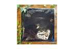A black Dragon Aromatherapy cloth or mat wrapped in clear plastic packaging, displayed on a wooden surface with green leaves around it. The packaging features the Dragon Aromatherapy logo.