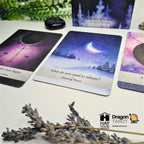 A tarot card deck set displayed on a light surface with decorative dried lavender and greenery. The main visible product is the tarot card deck, including cards and a box, with one central card showing a night sky and moon illustration.