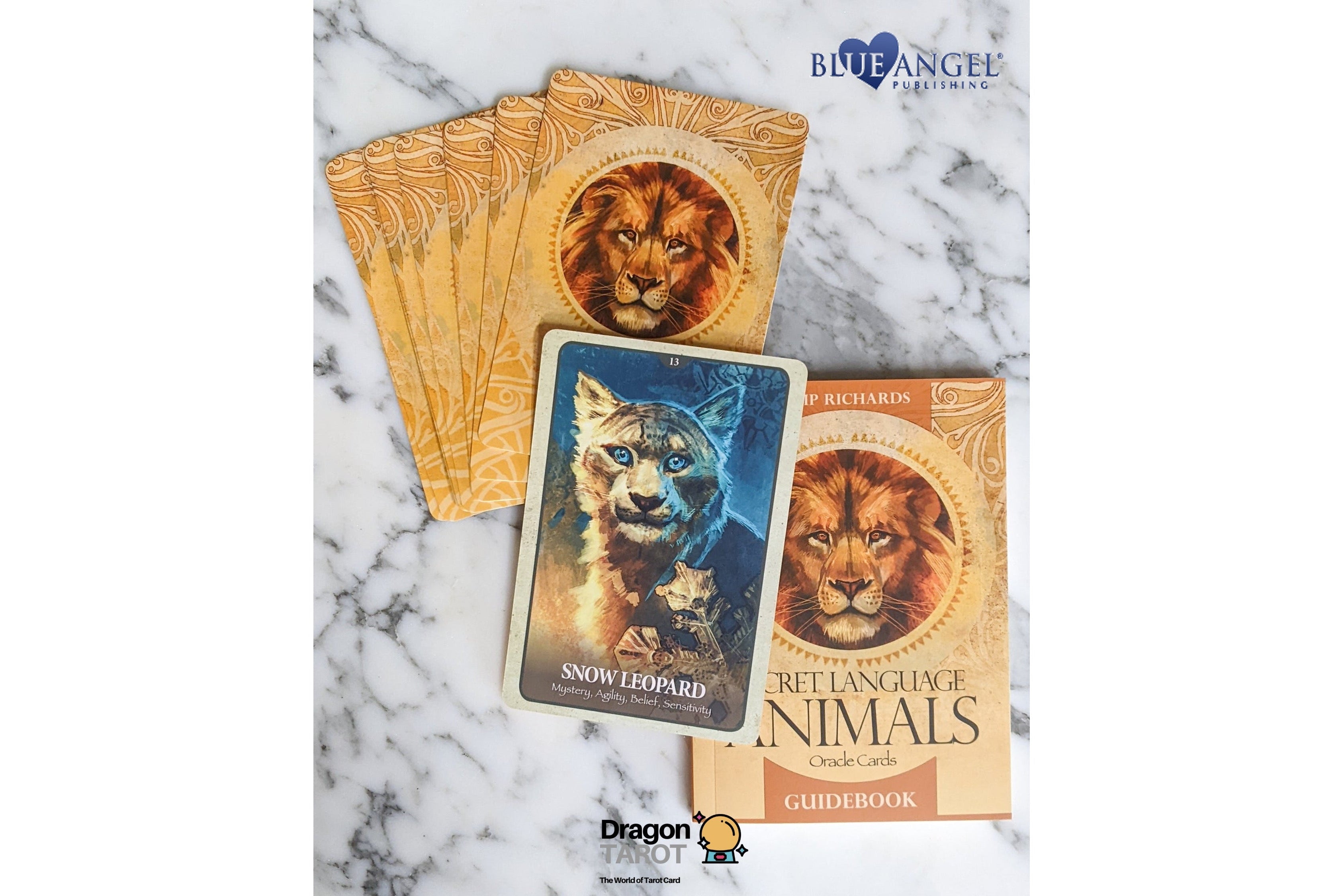 A tarot card deck and its guidebook displayed on a white marble background. The cards feature detailed animal illustrations, including a snow leopard and a lion, with gold-toned borders.