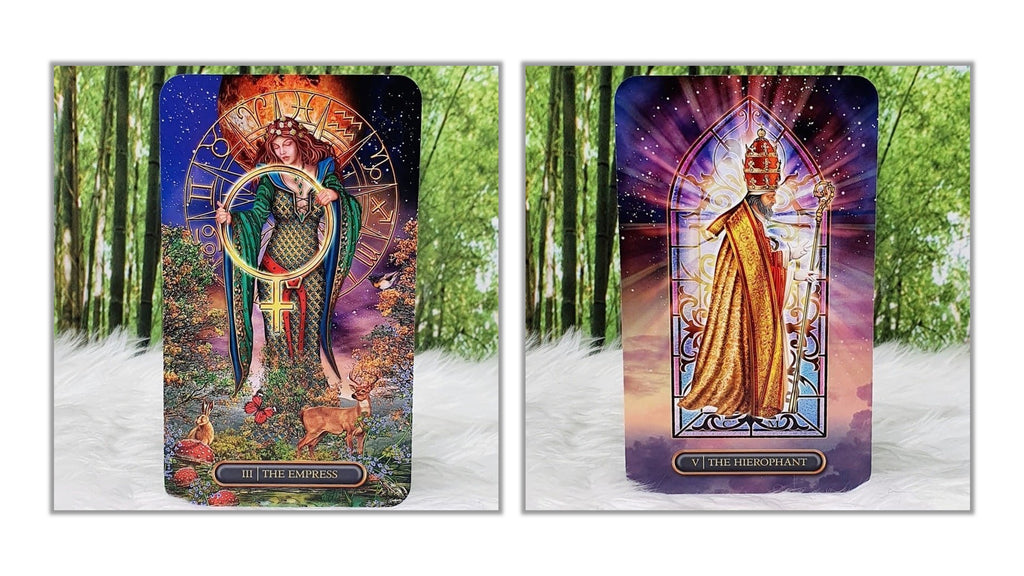 Two illustrated tarot-style cards shown side by side on a white furry surface with a blurred green forest background. The left card depicts a crowned woman in a green cloak holding a staff, with the text 'ALL THE POWER'.