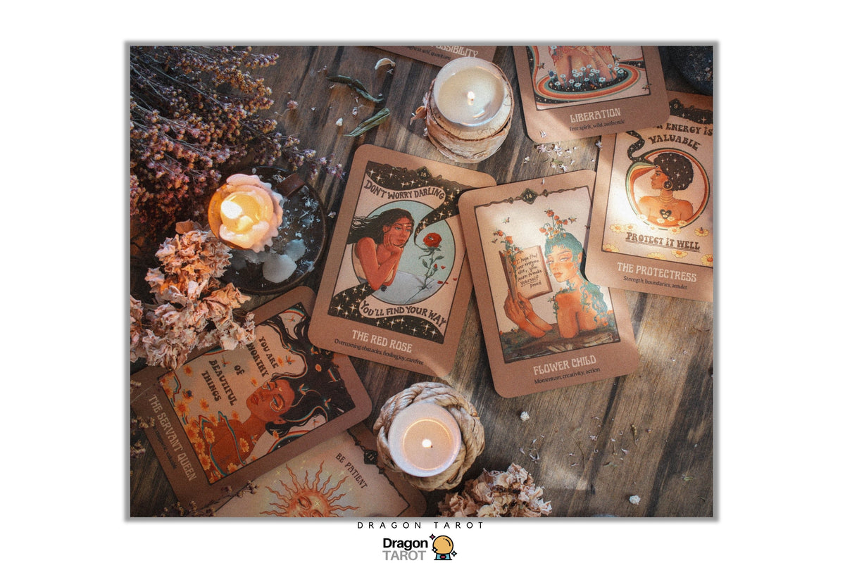 A flat-lay arrangement of illustrated tarot cards on a rustic wooden surface, surrounded by lit candles, dried flowers, and small decorative props. The cards feature vintage-style artwork with warm brown, beige, orange, and muted blue tones.