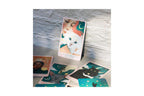 A boxed card deck standing upright on a tabletop, with several illustrated cards spread out in front. The box shows a white cat and the title 'A CAT'S DEPTH'.