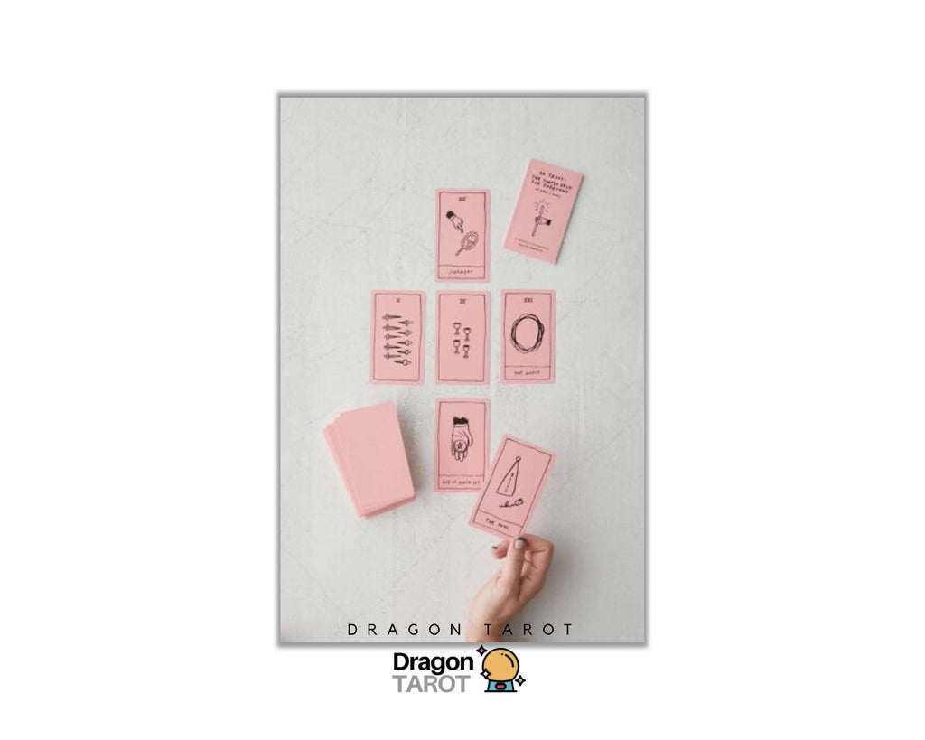 A flat-lay view of a Dragon Tarot deck on a light gray textured surface, showing several pink cards and a pink box, with a hand reaching in to pick up one card. The brand logo 'Dragon Tarot' is visible at the bottom of the image.