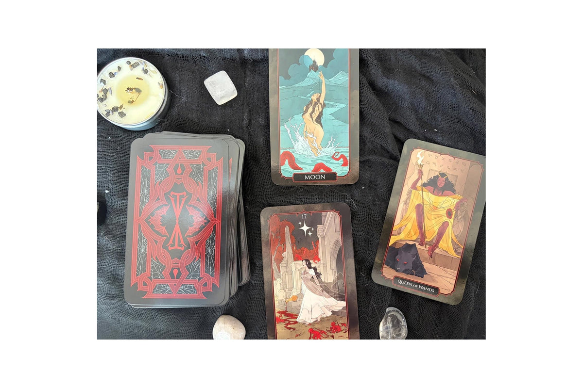 A tarot card deck with several illustrated cards laid out on a dark fabric surface, alongside small crystals and a round decorative object.
