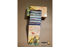 A boxed card game set labeled 'The Little Prince' with a stack of illustrated cards standing in front of the box on a brown surface. A small 'Dragon' logo appears in the lower right corner.