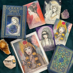 Goddess Spirit Oracle Deck box and several illustrated oracle cards arranged on a dark teal fabric background, with crystals and a small Dragon 97 logo stone nearby.