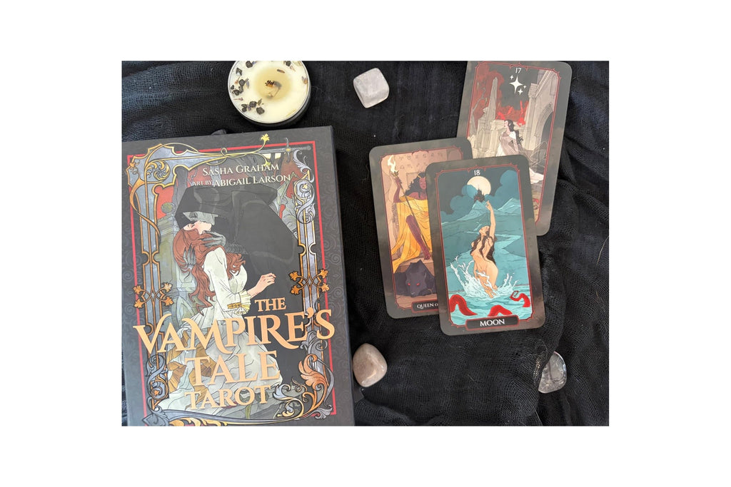 The Vampire's Tale Tarot deck by Sarah Grafton, displayed with its illustrated box on a black fabric background alongside three fanned tarot cards and small decorative stones and a candle.