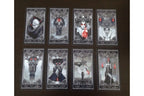 Eight gothic tarot cards arranged in two rows of four on a dark brown wooden surface. The cards feature dark, moody illustrations of hooded figures, skulls, and red accents, with ornate silver-gray borders.