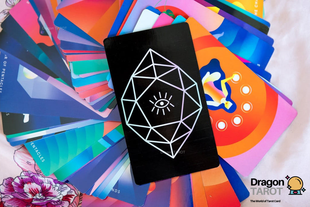 A black tarot card featuring a white geometric eye design, fanned out over a vibrant assortment of colorful tarot cards. The Dragon Tarot logo is visible in the bottom right corner.