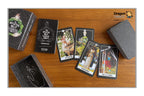 A tarot card deck set displayed on a wooden tabletop, including a textured black box, a deck of cards, several illustrated cards fanned out, and a gray card holder. The Dragon Tarot logo is visible in the top right corner.