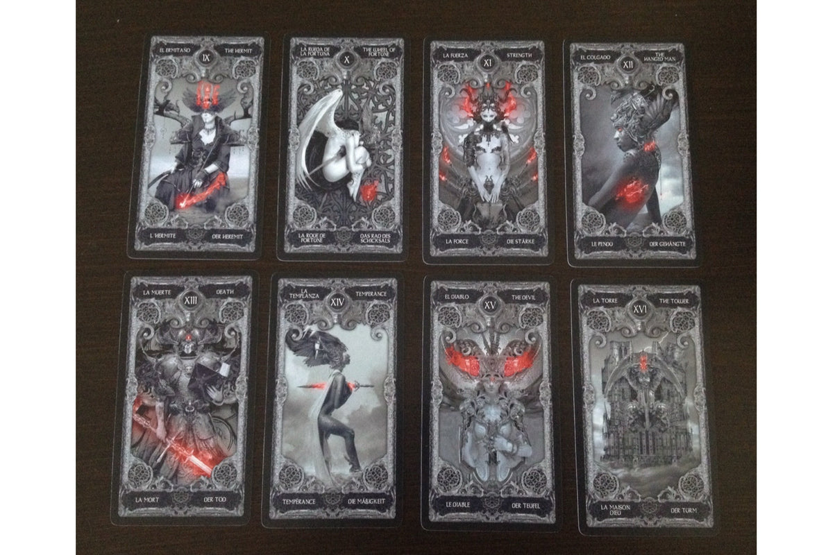 Eight gothic tarot cards arranged in two rows of four on a dark wooden surface, featuring black and gray illustrations with red accents.