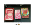 Dragon Tarot card deck set including a red box with pink cloud-patterned interior, a pink card in the center, and the 'Goddess of Love Tarot' book on a dark surface.