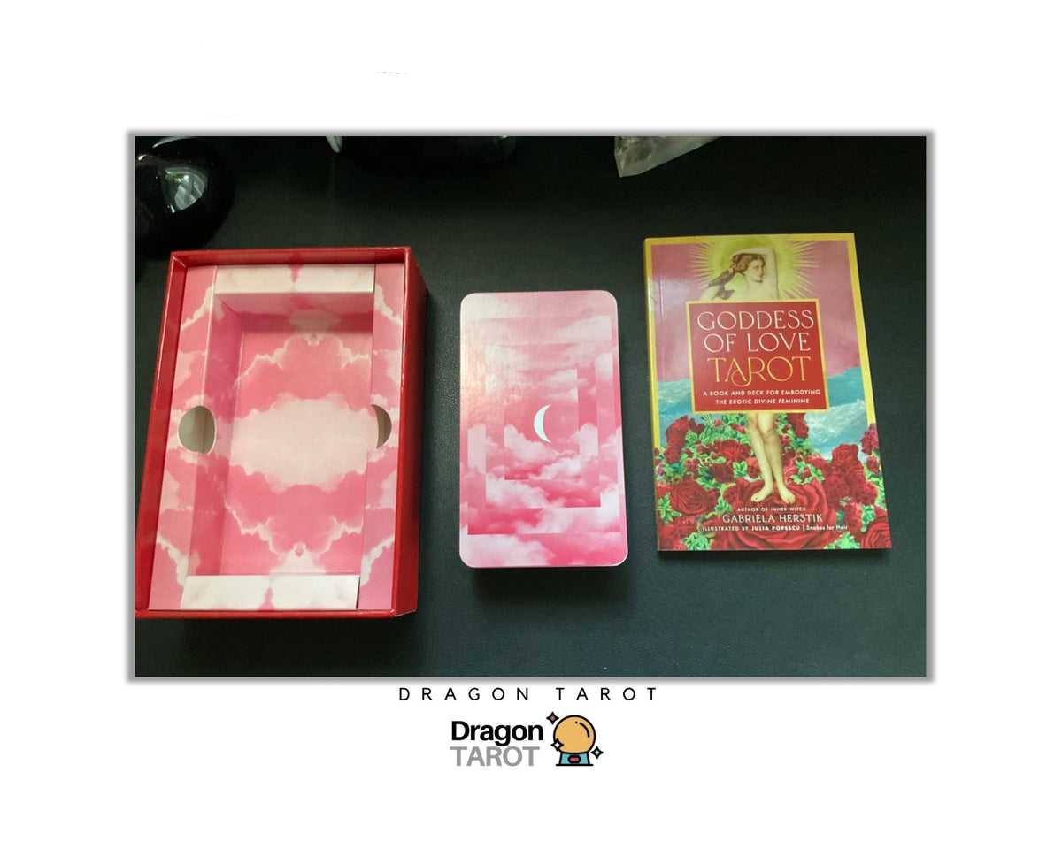 Dragon Tarot card deck set including a red box with pink cloud-patterned interior, a pink card in the center, and the 'Goddess of Love Tarot' book on a dark surface.