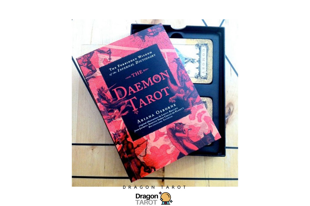 The Daemon Tarot deck by Ariana O'Donoghue, featuring a red and black illustrated book-style box placed on top of the tarot cards inside a black tray, photographed on a light wood surface.