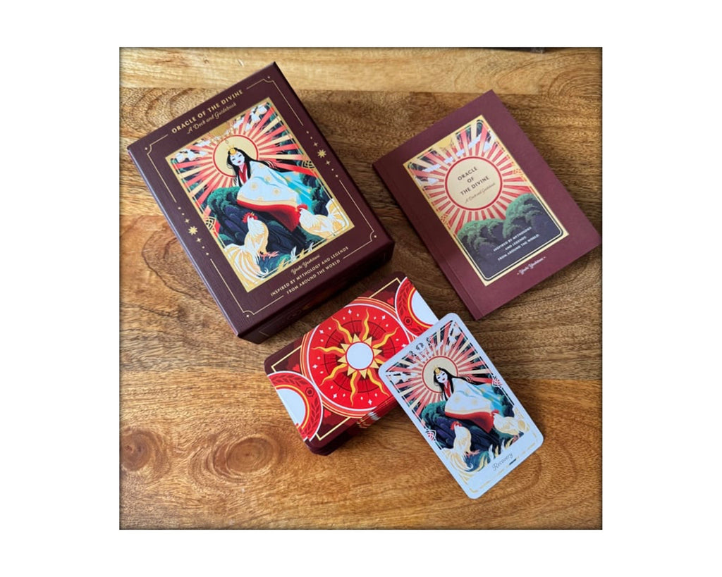 A boxed card deck and two cards displayed on a wooden surface. The packaging and card backs feature a dark reddish-brown border with a central religious illustration of a haloed figure and a red sunburst design.