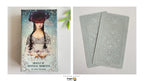 Oracle of Mystical Moments tarot deck by Carrie Wade-Stein, showing the illustrated front cover on the left and two back-facing cards with ornate pale blue-gray designs on the right, photographed on a light neutral background.