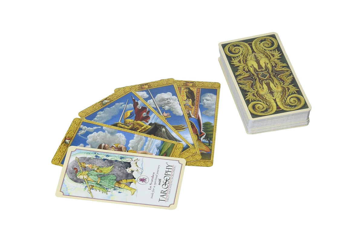 A tarot card deck with one card fanned out and another face-up card in front, alongside a stacked deck with ornate gold and black back art, on a plain white background.