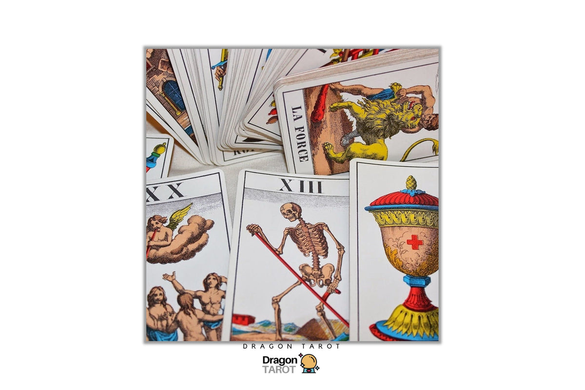 A set of illustrated tarot cards fanned out on a white background, with several cards fully visible including the Three of Swords, Eight of Cups, and The Hanged Man. The Dragon Tarot logo is visible at the bottom.