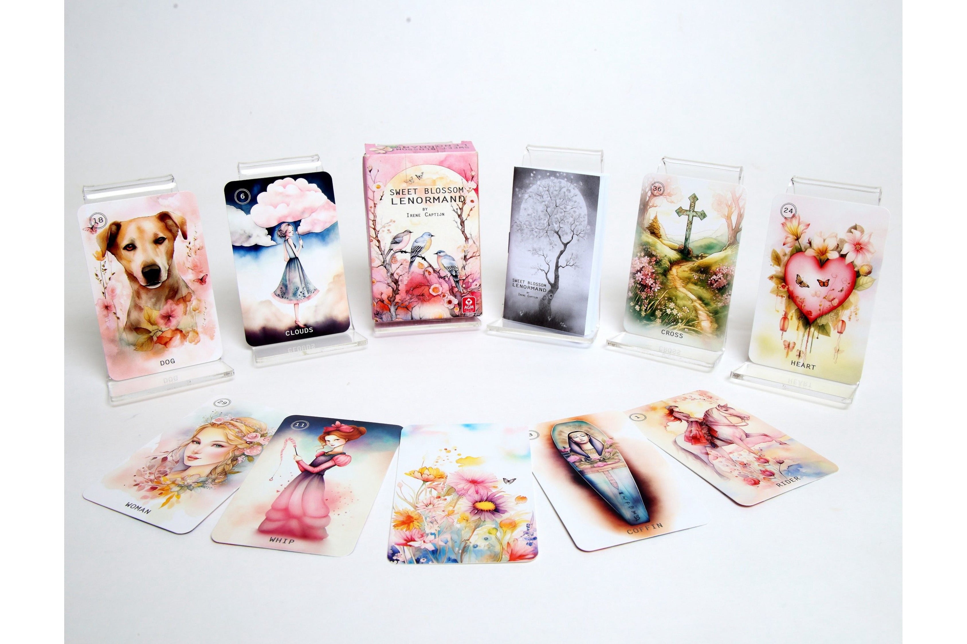 A set of illustrated oracle or tarot-style cards displayed on a white background, with several cards standing upright in clear acrylic holders and others fanned out in front. The cards feature pastel watercolor-style artwork including a dog, a woman under a pink umbrella, floral scenes, a tree, a cross, and a heart motif.